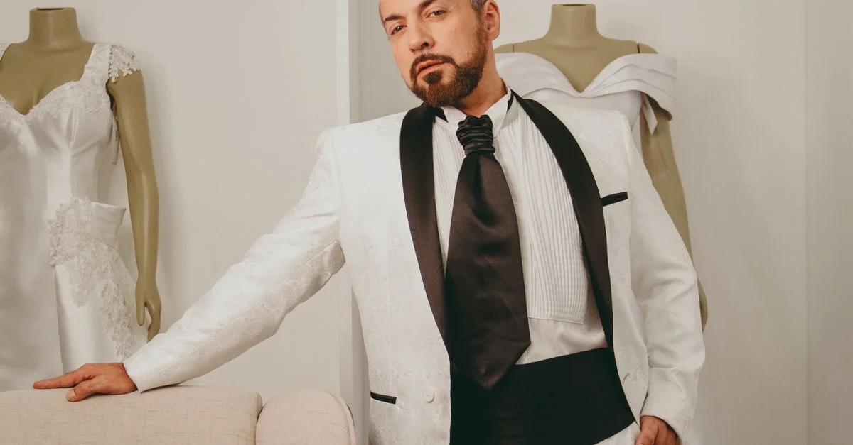 Un homme en tuxedo blanc élégant se tient avec confiance dans un studio, entouré de mannequins.